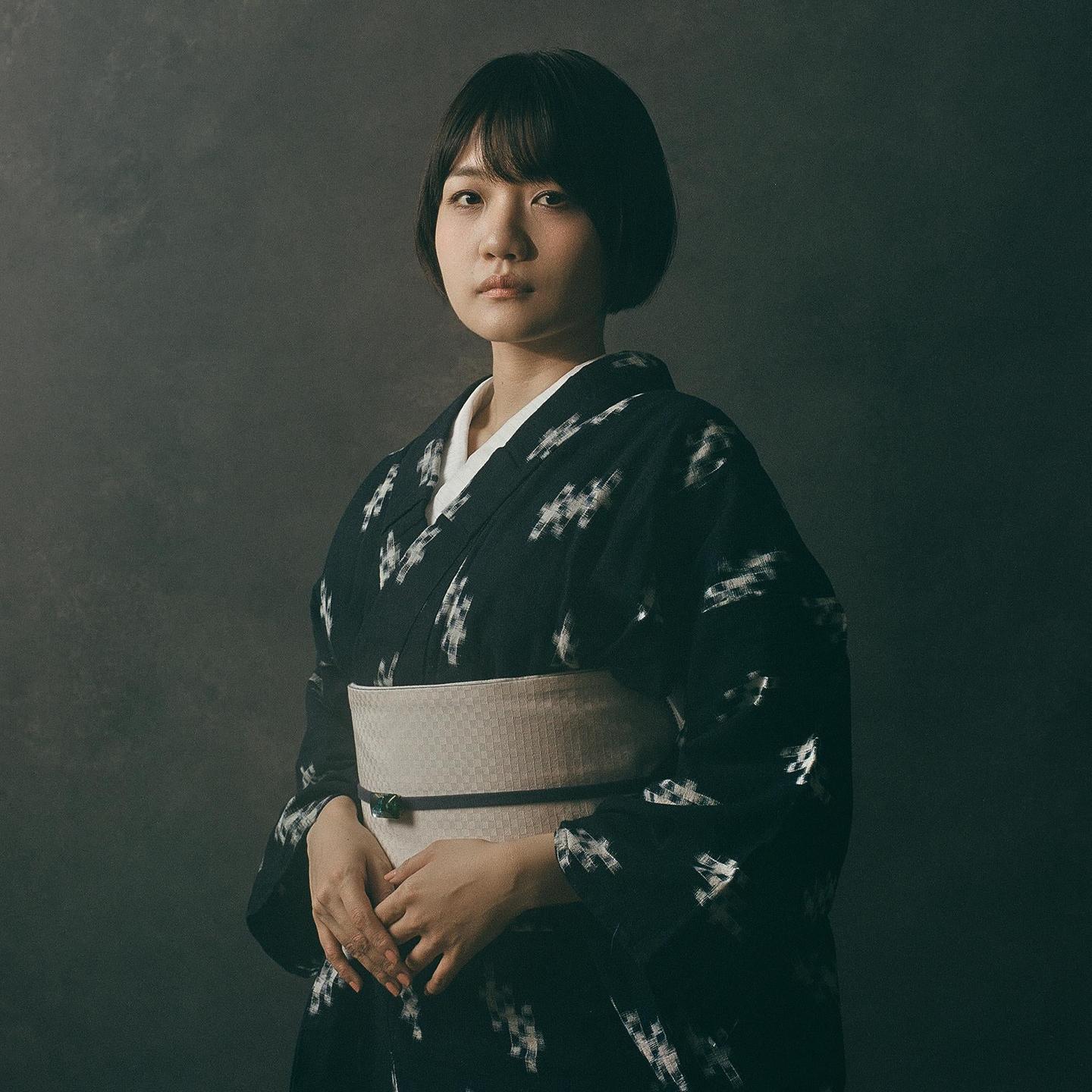 A woman with short hair wears a patterned kimono and obi.
