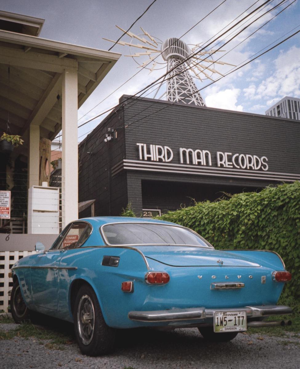 A blue car is parked in front of a building with "Third Man Records" written on it, and a Tesla coil sculpture is visible on the roof.