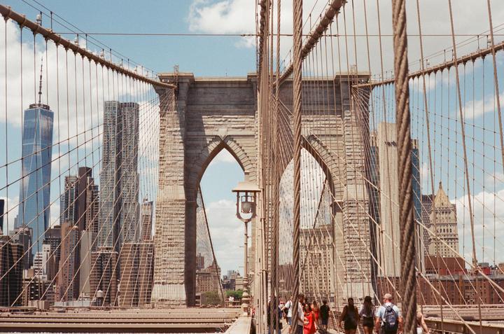 People walk across the Brooklyn Bridge with the New York City skyline in the background.
