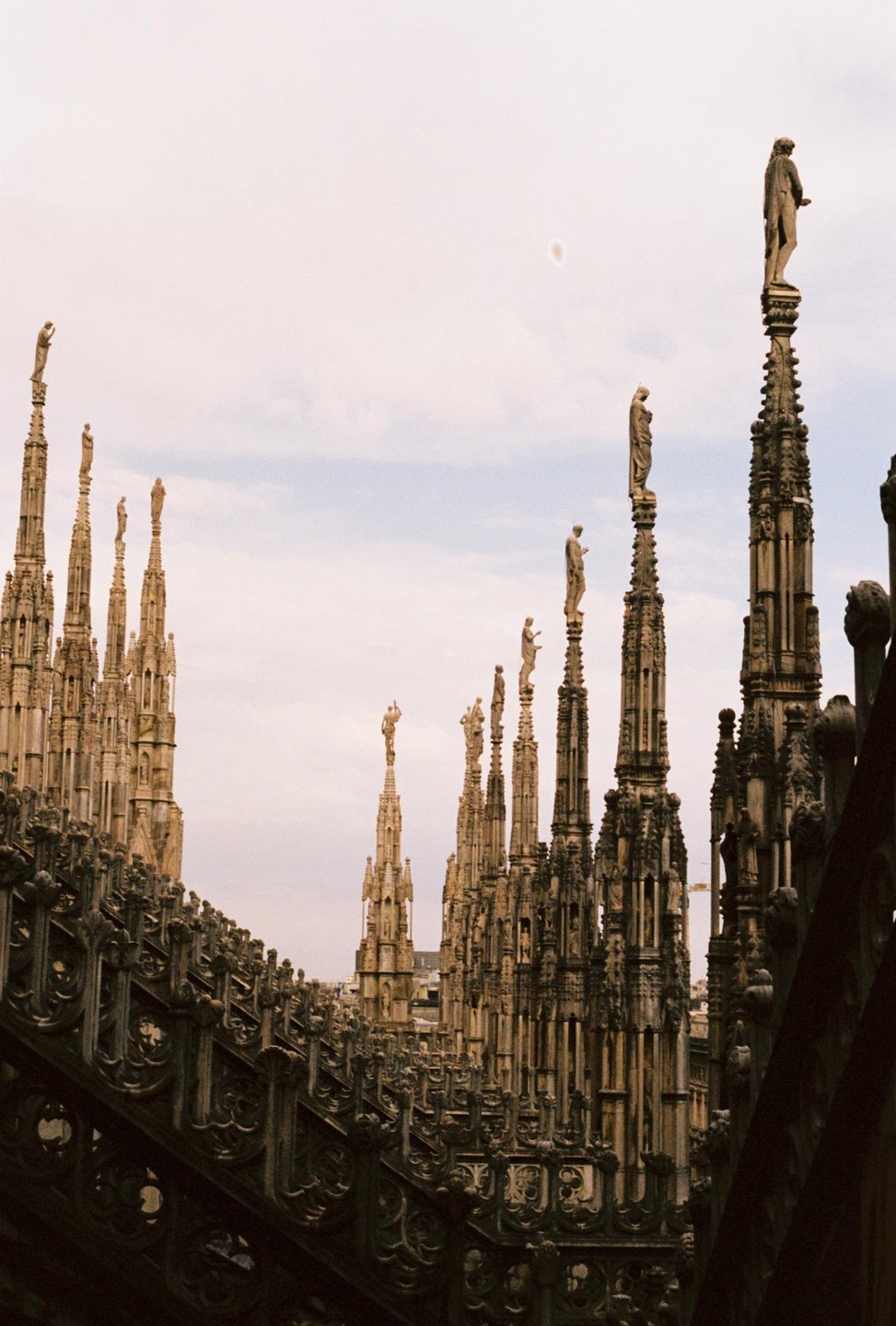 A low-angle view shows the ornate spires and statues of the Duomo against a cloudy sky.