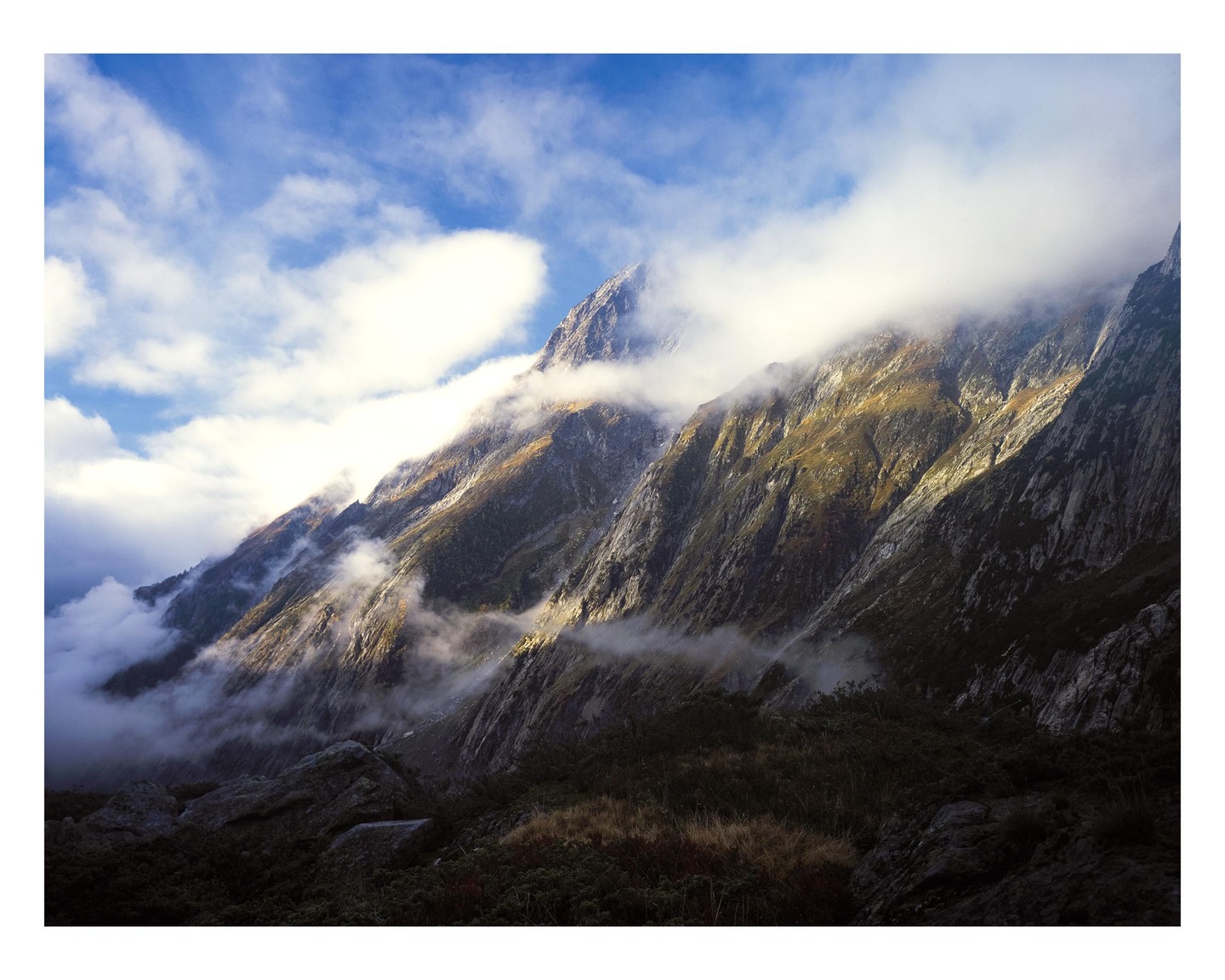 Clouds partially obscure a rugged mountain landscape with patches of sunlight illuminating the slopes.