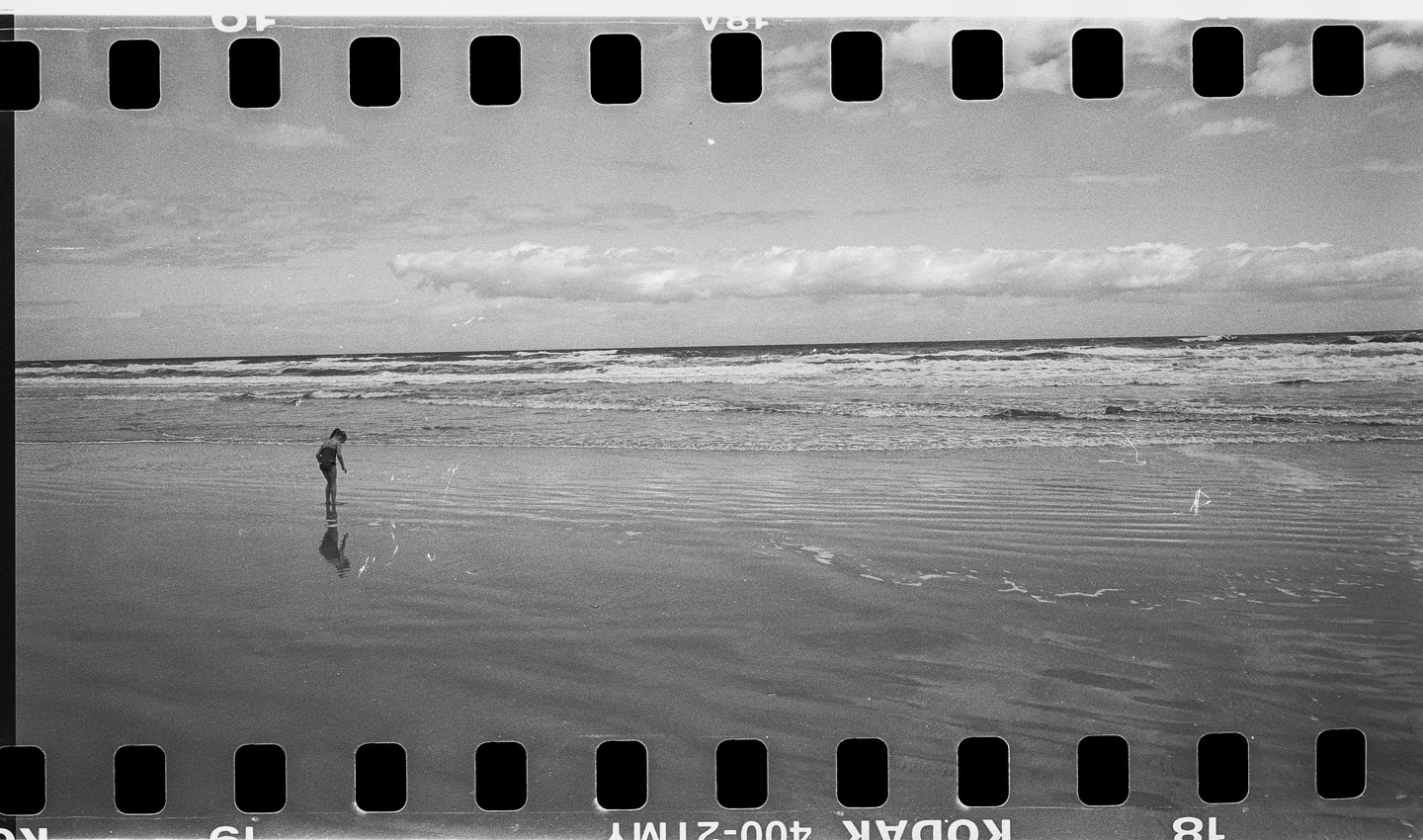 A child stands in the shallow water of a beach with waves crashing in the background.