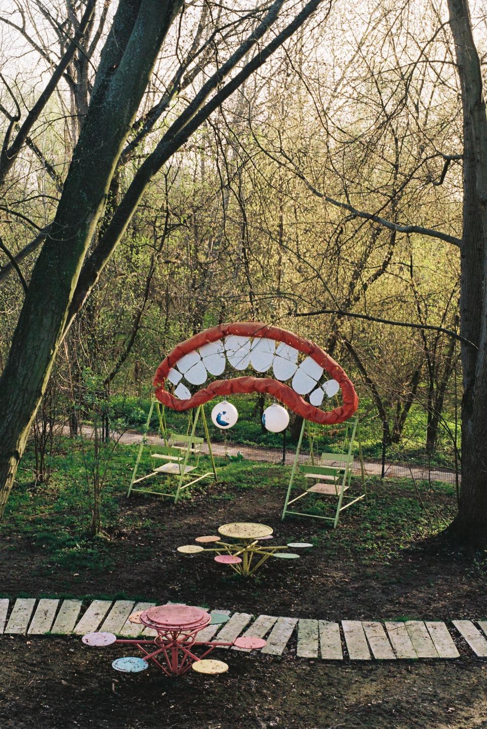 A whimsical playground structure shaped like a giant mouth with teeth and eyes is nestled among trees in a park.