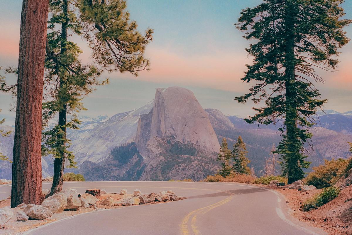 A winding road leads to a view of Half Dome in Yosemite National Park, framed by pine trees.