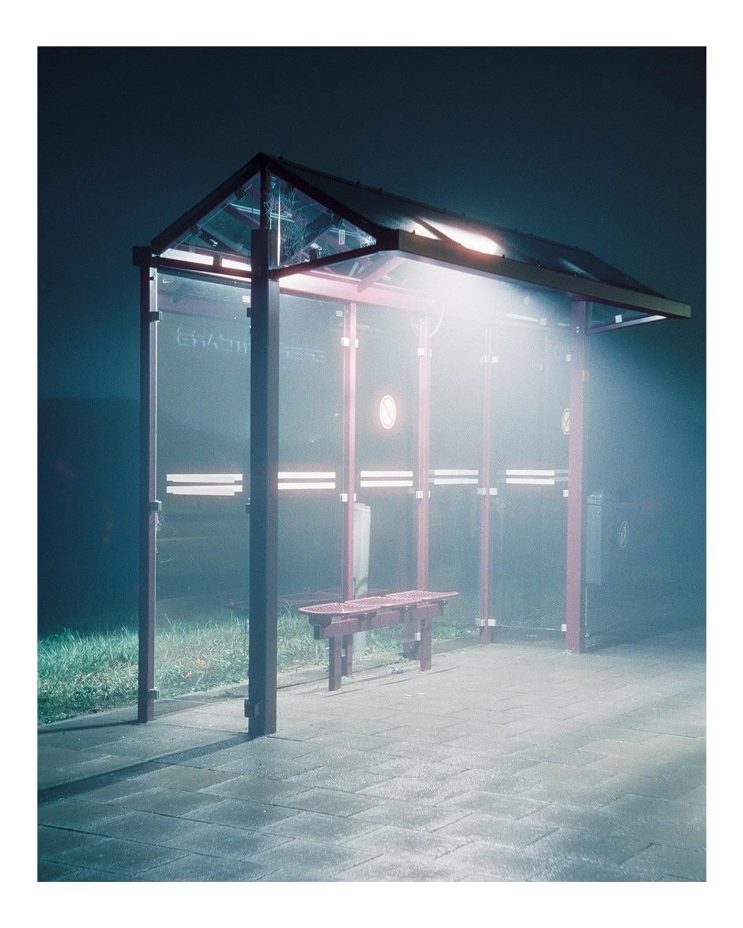 A brightly lit bus stop with a bench is visible at night.