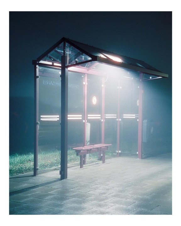 A brightly lit bus stop with a bench is visible at night.