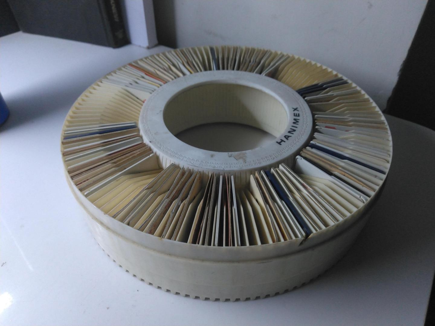 A circular slide tray filled with numerous photographic slides is visible on a white surface.