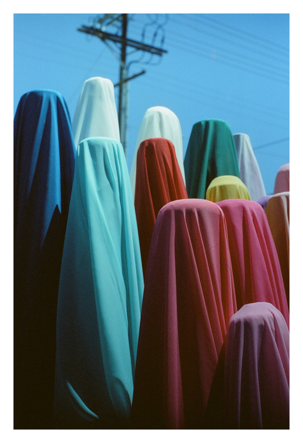 A collection of colorful draped fabrics stands under a clear blue sky with a utility pole in the background.