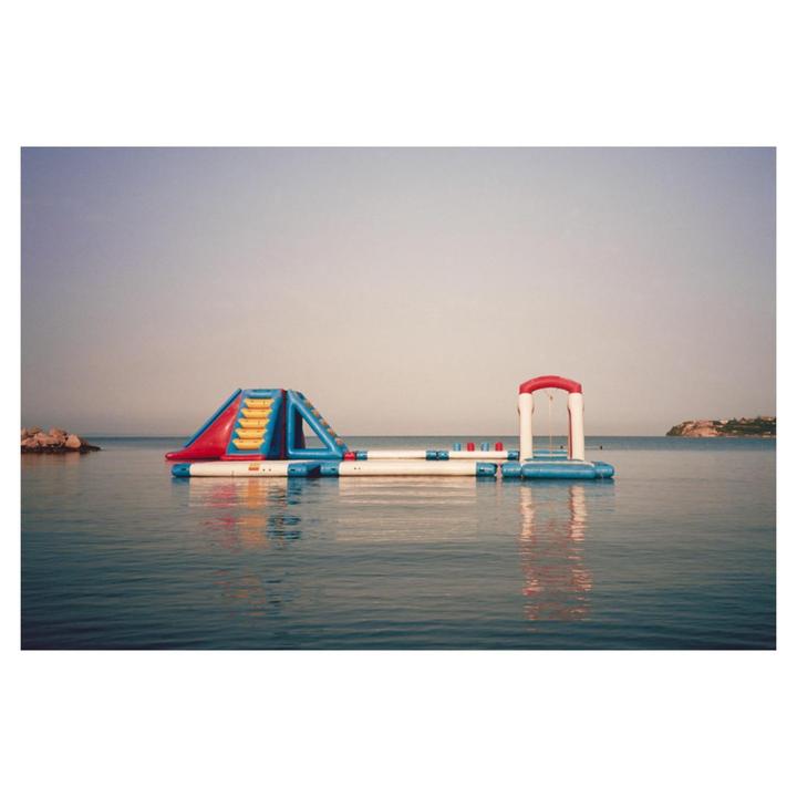An inflatable water park floats on calm water under a clear sky.