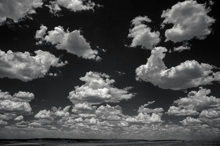 A wide shot shows a vast landscape under a sky filled with numerous cumulus clouds.