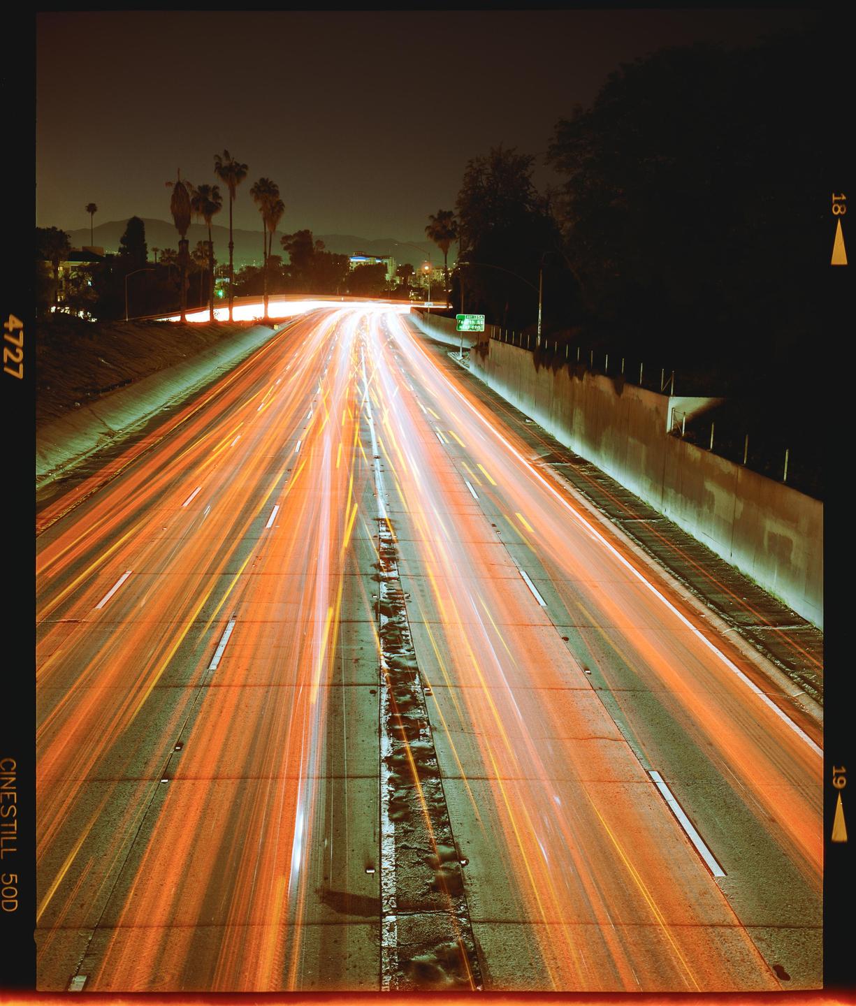 A long exposure photograph captures the light trails of vehicles on a highway at night.