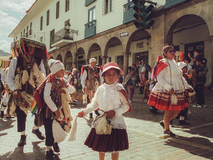 A group of people in traditional clothing walk down a street during a parade.