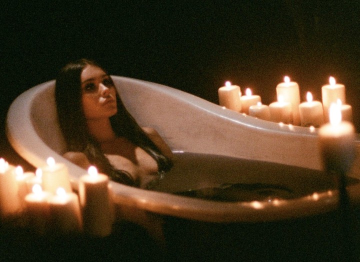 A woman is in a bathtub surrounded by many lit candles in a dark room.