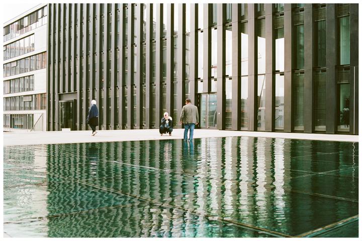 A man and a woman are near a reflective pool in front of a modern building.