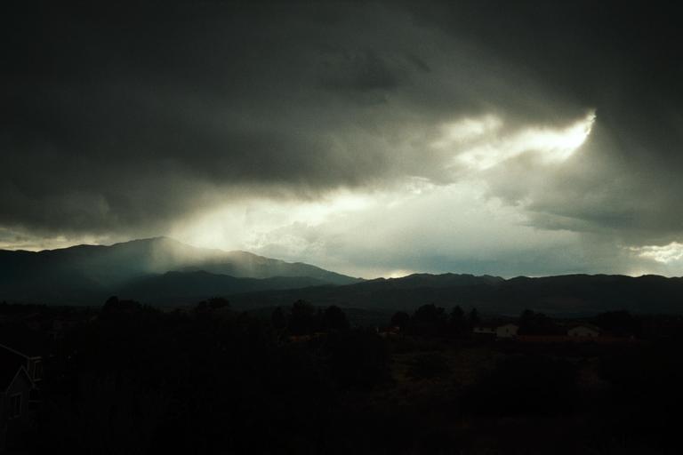 Sunlight breaks through dark clouds, illuminating a mountain range and a valley with scattered houses.