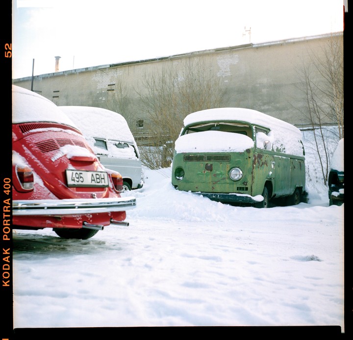 A red car and a green van are parked in a snowy lot next to a building.