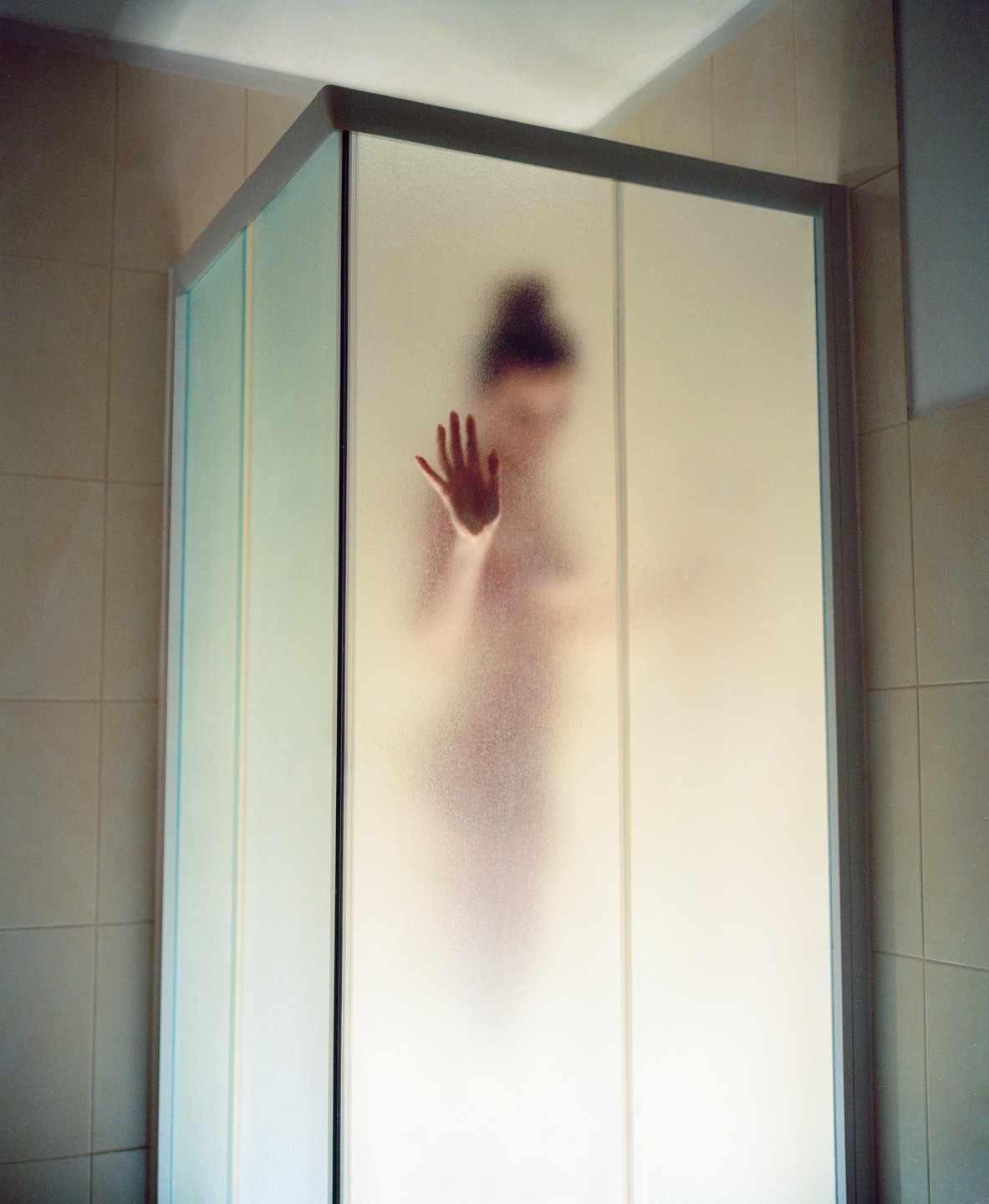 A blurred figure of a woman is visible behind the frosted glass of a shower cabin, with her hand pressed against the glass.