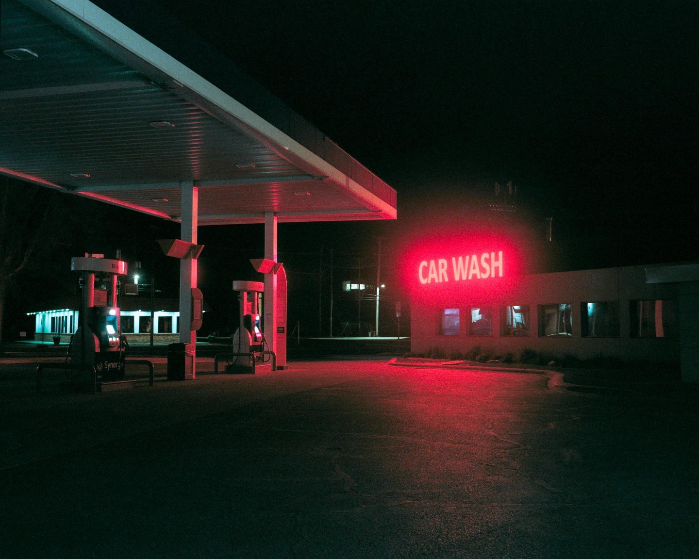 A gas station with a red neon car wash sign is illuminated at night.