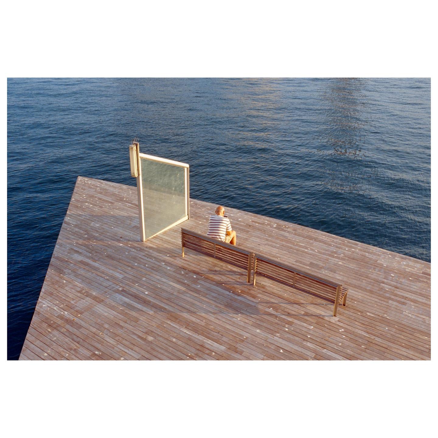 A man sits on a wooden bench on a pier next to the water.