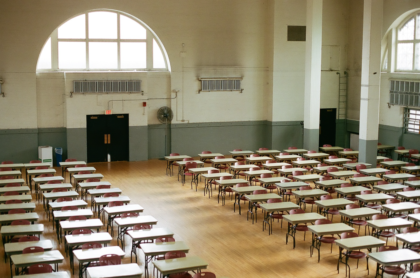 An empty hall is filled with rows of tables and chairs, ready for an exam.