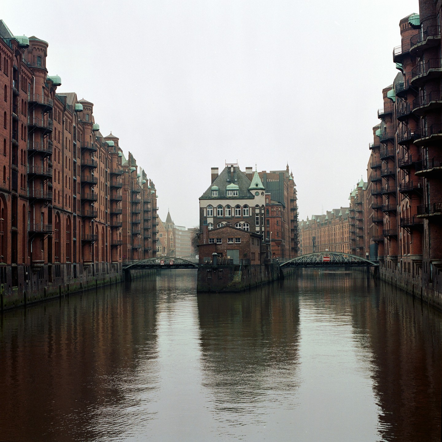 A canal flows between tall brick buildings with bridges connecting the two sides.