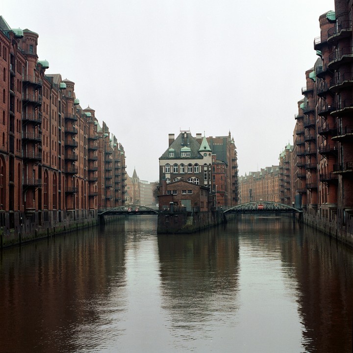 A canal flows between tall brick buildings with bridges connecting the two sides.