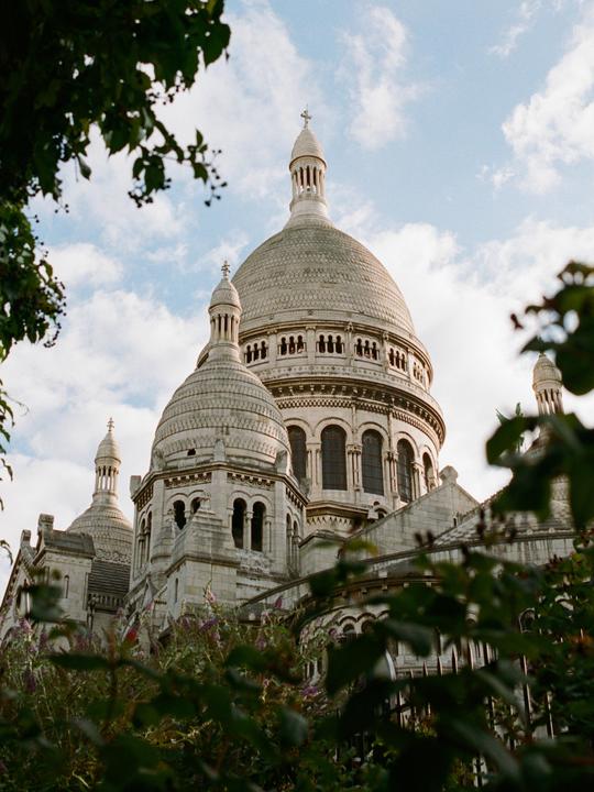 The Sacre Coeur basilica is partially visible through green foliage.