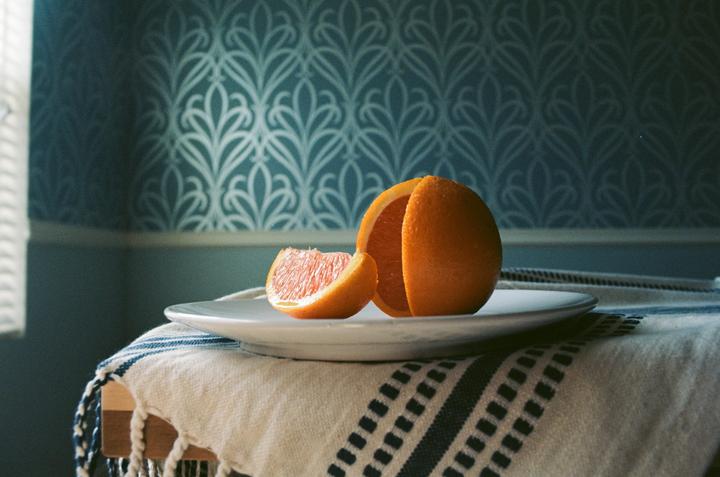 A partially peeled orange and a slice of orange rest on a white plate, which is on a striped cloth.