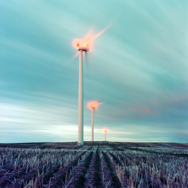 Three wind turbines with glowing orange lights on their blades stand in a field under a streaky blue sky.