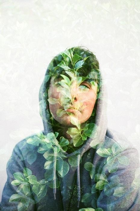 A man in a hoodie is shown in a double exposure with green leaves.