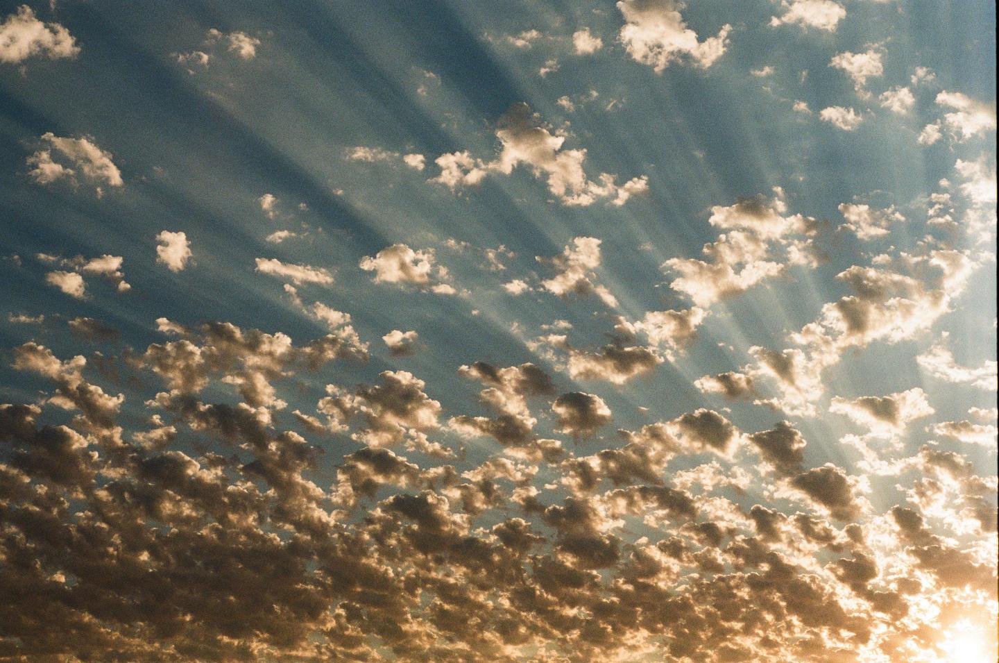 Sunlight streams through a partly cloudy sky, illuminating the clouds from below.