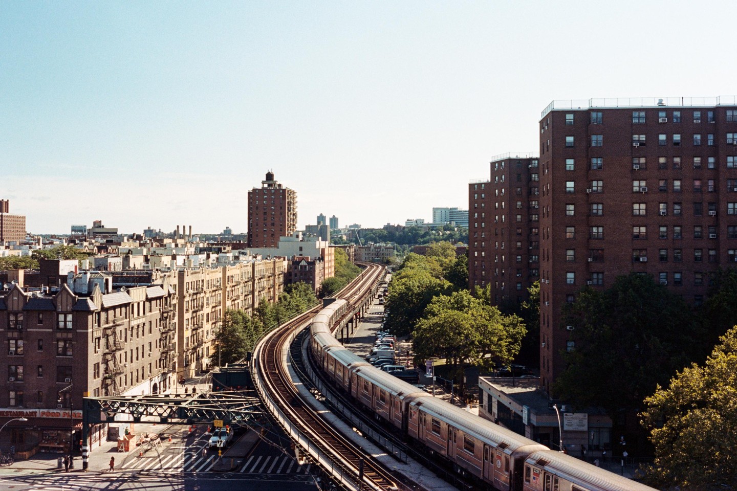 A train travels on elevated tracks through a city with tall buildings and trees.