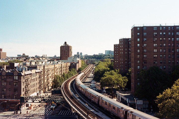 A train travels on elevated tracks through a city with tall buildings and trees.