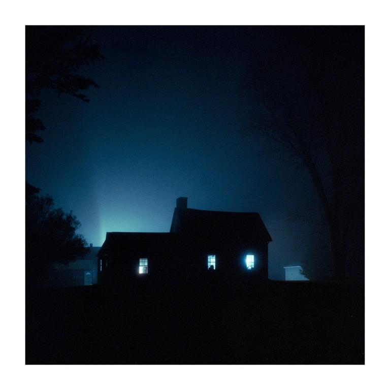 A dark house with illuminated windows stands against a deep blue night sky.
