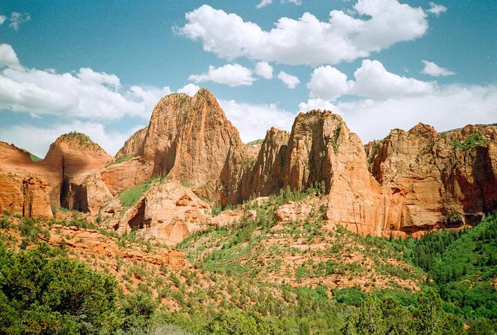 A wide shot shows the red rock formations of Kolob Canyons under a blue sky with white clouds.