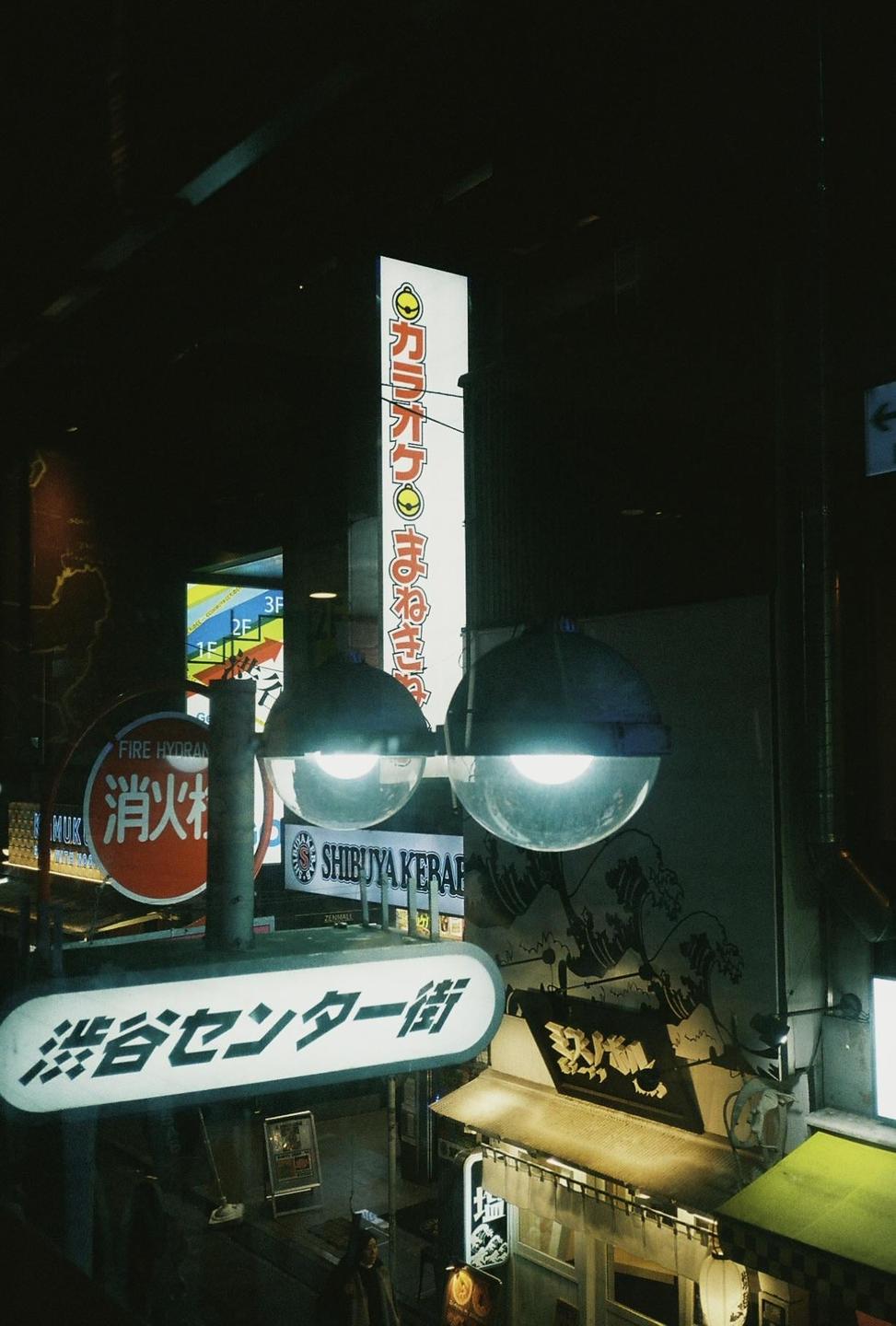 A street scene at night shows illuminated signs and streetlights above a building with a wave mural.