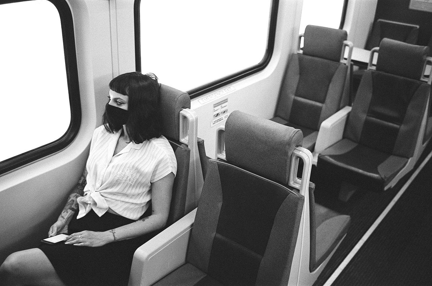 A woman wearing a face mask sits alone on a train and looks out the window.