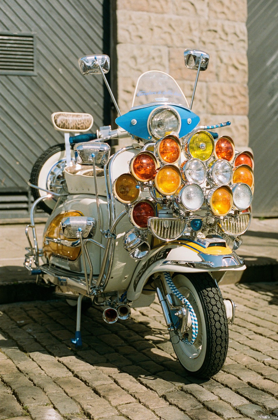 A highly customized scooter with many lights and chrome details is parked on a cobblestone street.