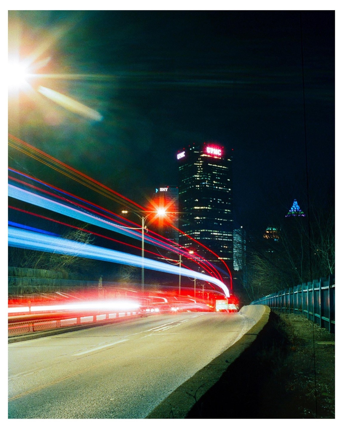 Light trails from vehicles on a road at night with a tall building in the background.