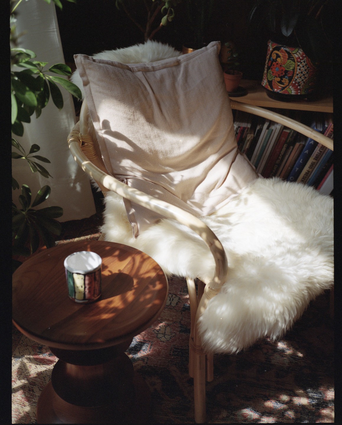 Sunlight illuminates a cozy chair with a sheepskin throw and a small wooden table with a colorful mug.