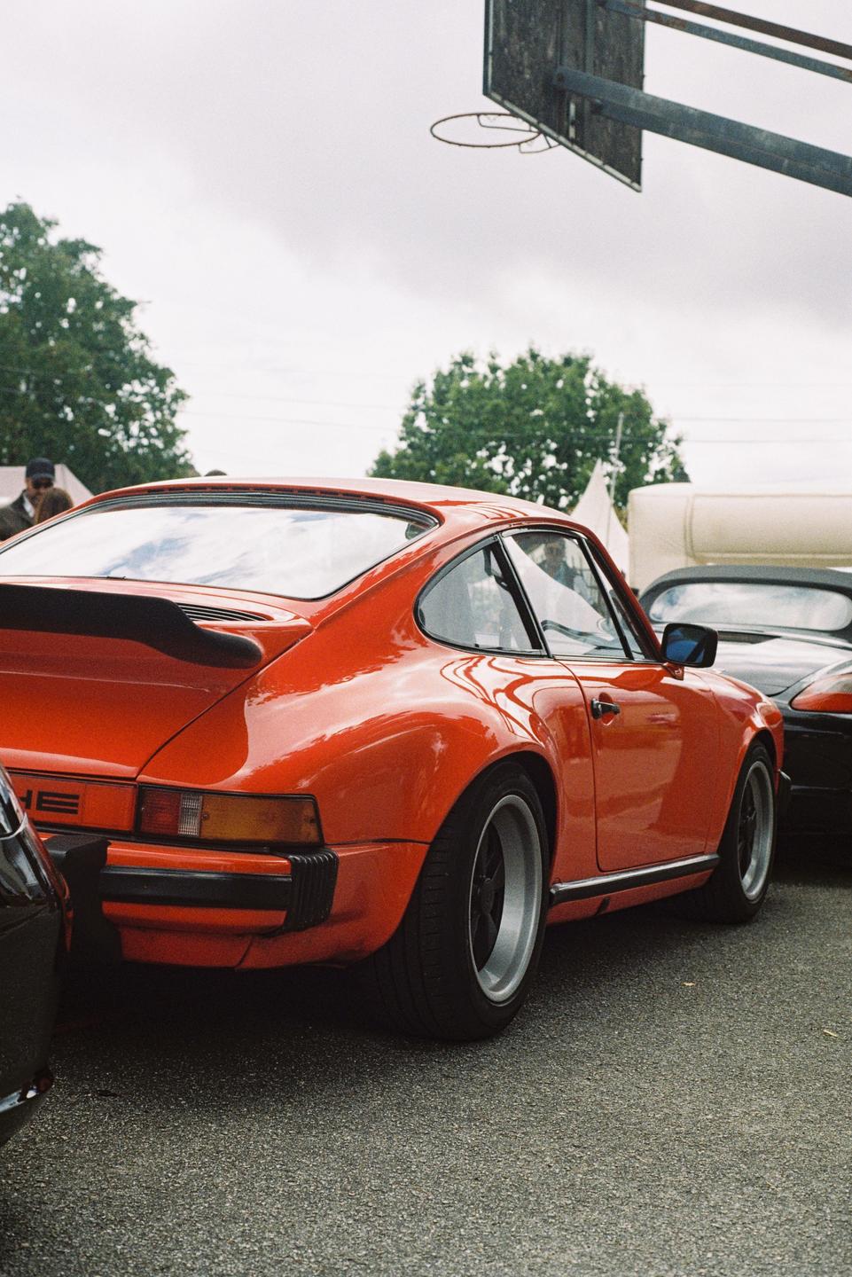 An orange sports car is parked on asphalt next to another vehicle under a cloudy sky.