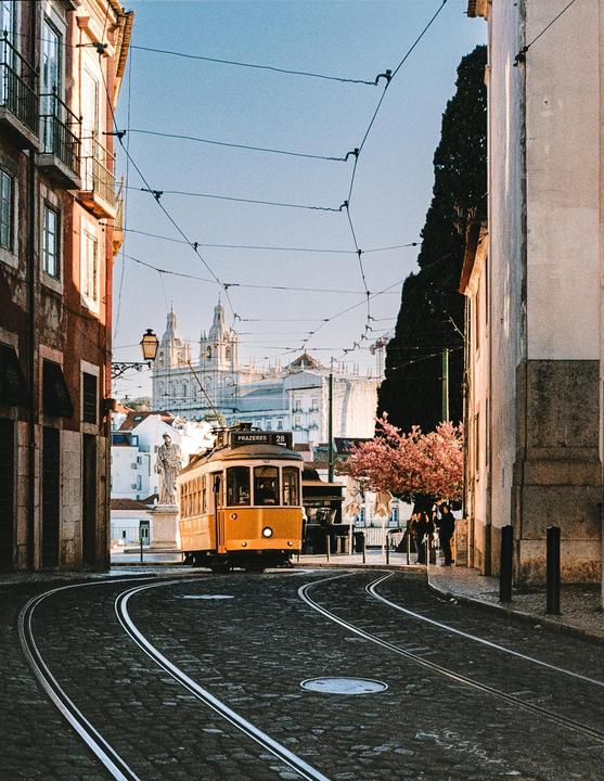 A yellow tram travels on a cobblestone street with buildings and a church in the background.