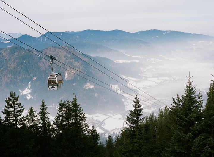 A gondola travels over a forest with a hazy mountain valley in the background.