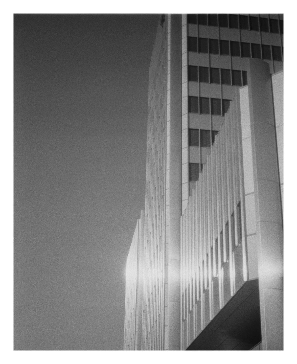 A tall building with many windows is shown from a low angle, with a bright light reflecting off its side.