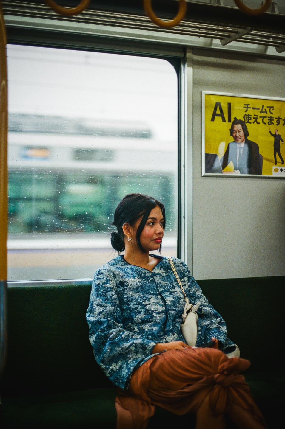 A woman sits on a train looking out the window, with an advertisement for AI visible on the wall.