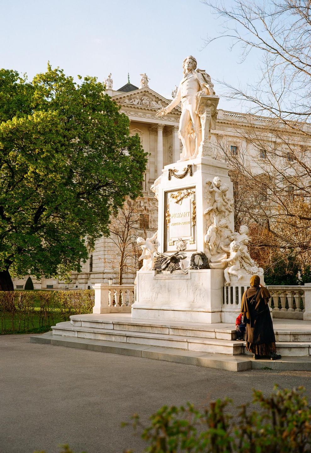 A woman and child stand before the Mozart monument in Vienna.