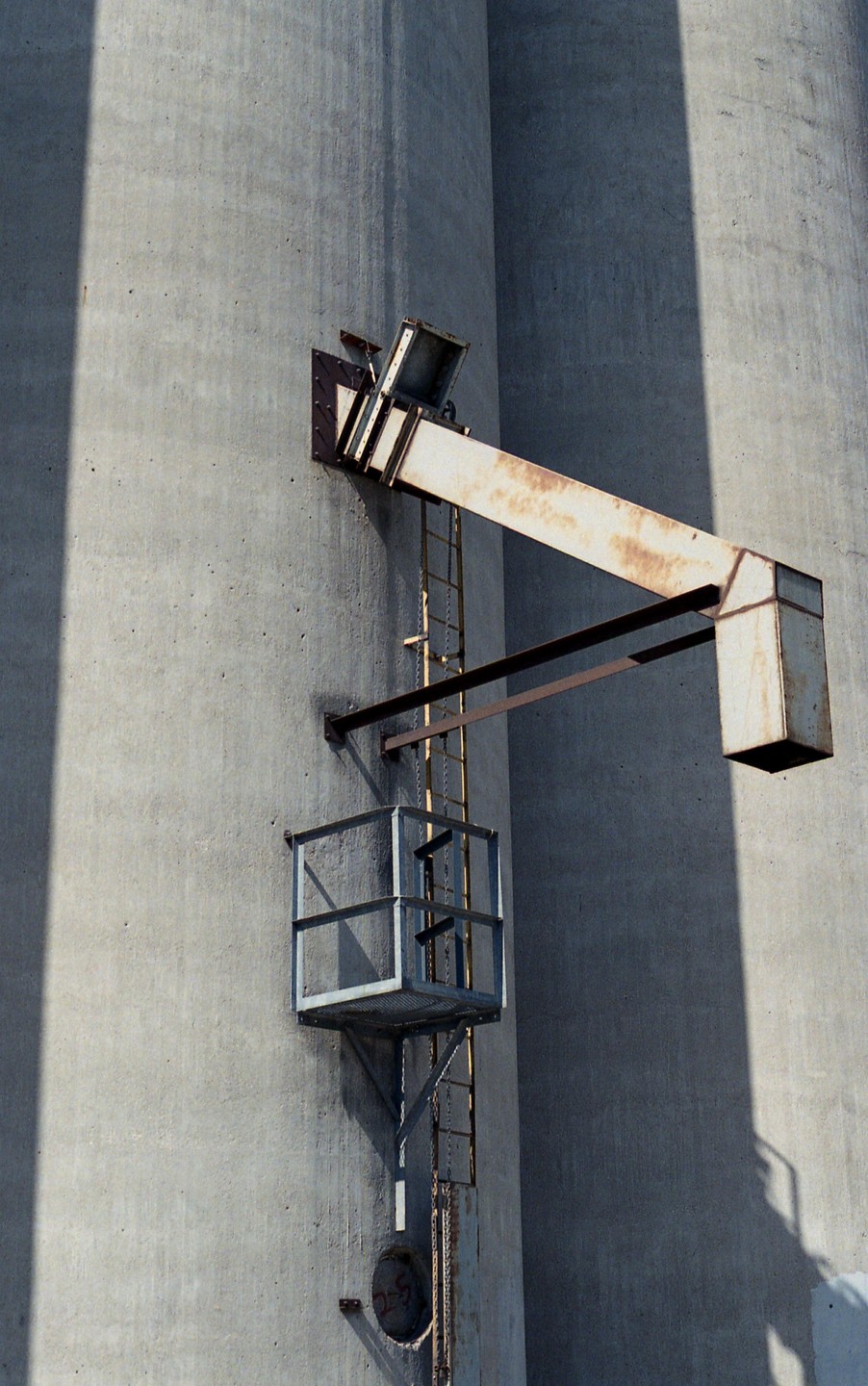 A metal ladder and platform are attached to a concrete grain silo.
