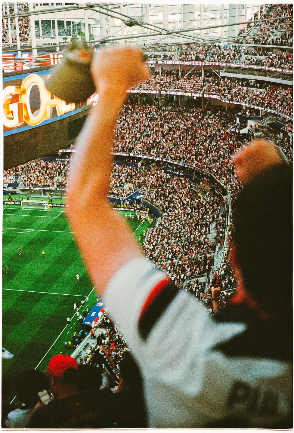 A person raises their arm in a crowded stadium during a soccer match.