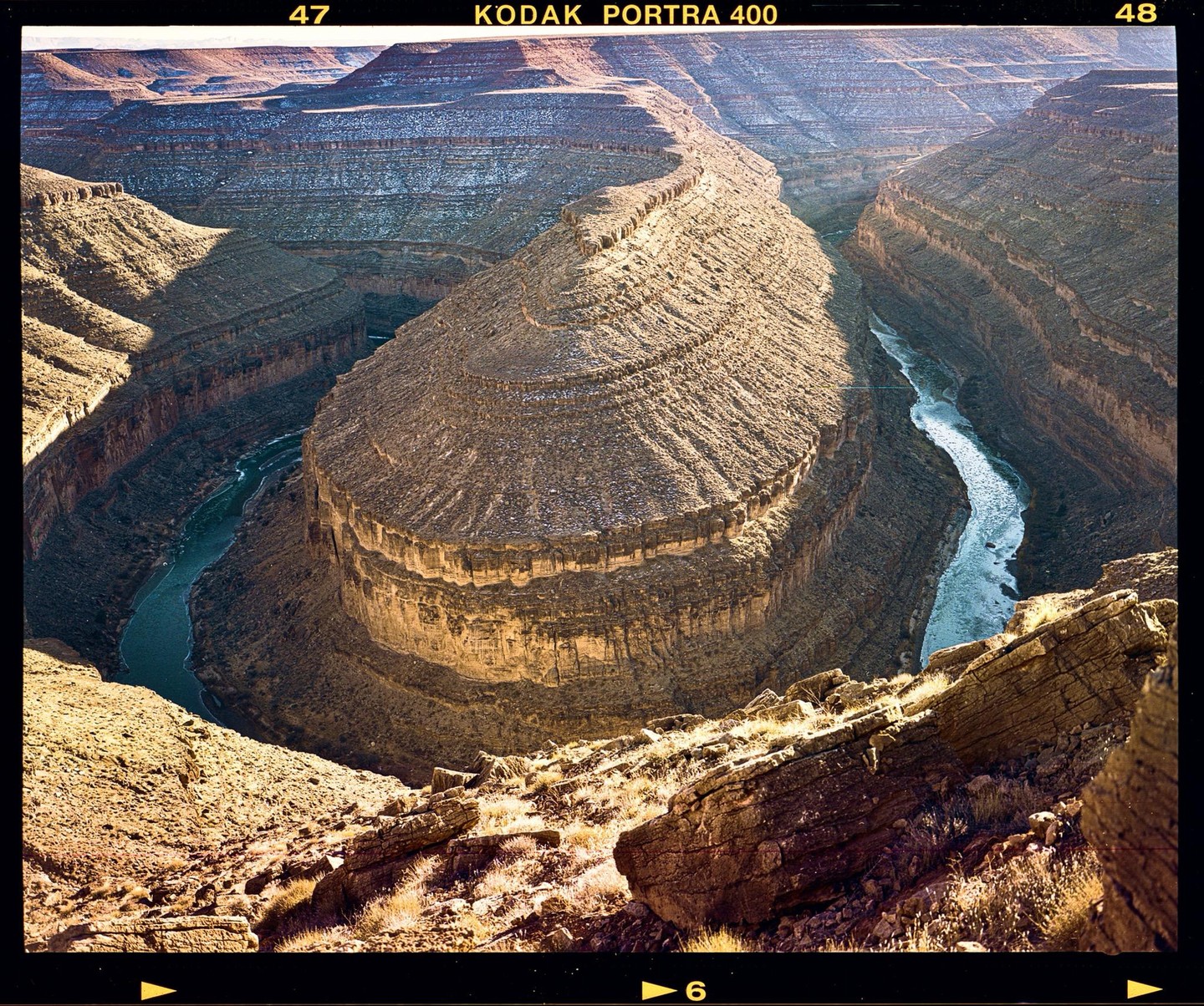 A winding river cuts through a deep canyon with layered rock formations under a bright sky.