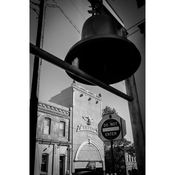 A large bell hangs above a street with a "Do Not Enter" sign and a building with "Liberty" inscribed on it.